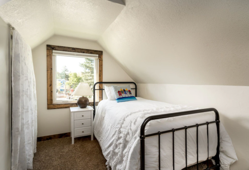Cozy bedroom with a single bed, white bedding, a nightstand, and a window with a view of trees outside.