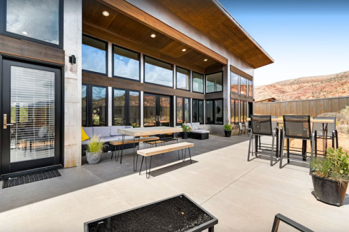 Modern outdoor patio with seating, large windows, and mountain views in a sunny setting.
