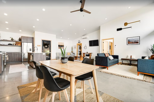 Modern open-concept living space with a dining table, kitchen, and cozy seating areas, featuring natural light and minimalist decor.
