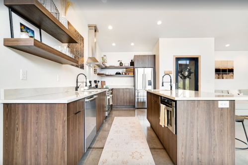 Modern kitchen with wooden cabinets, white countertops, and stainless steel appliances, featuring open shelving and a rug.