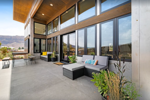 Modern outdoor patio with seating, plants, and large windows overlooking a scenic landscape.