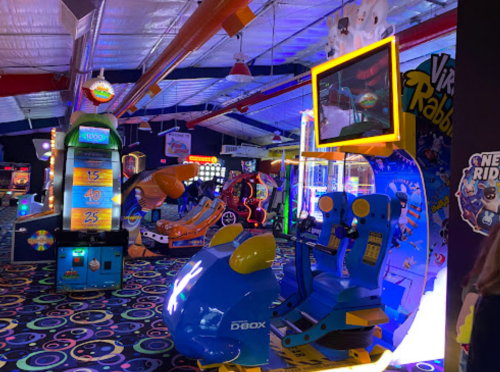 A vibrant arcade filled with colorful games and neon lights, featuring various machines and seating areas.