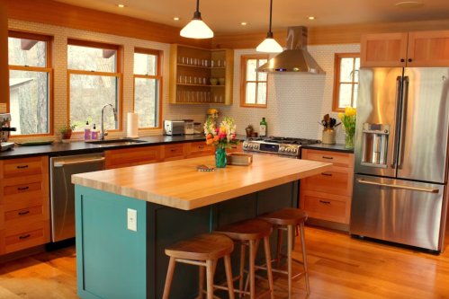 Modern kitchen with wooden cabinets, a large island, stainless steel appliances, and natural light from multiple windows.