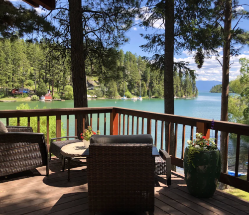A serene lakeside view from a wooden deck, featuring comfortable seating and lush greenery surrounding the water.