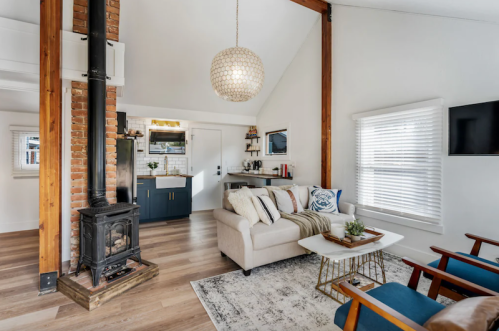 Cozy living room with a fireplace, modern decor, and large windows, featuring a sofa and wooden furniture.