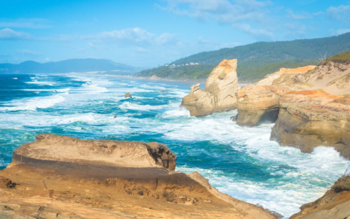 A scenic coastal view with rocky cliffs, crashing waves, and a blue sky, showcasing the beauty of the ocean.
