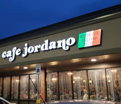 Exterior of Cafe Jordano, an Italian restaurant, with a sign and colorful flag, bustling with diners inside.