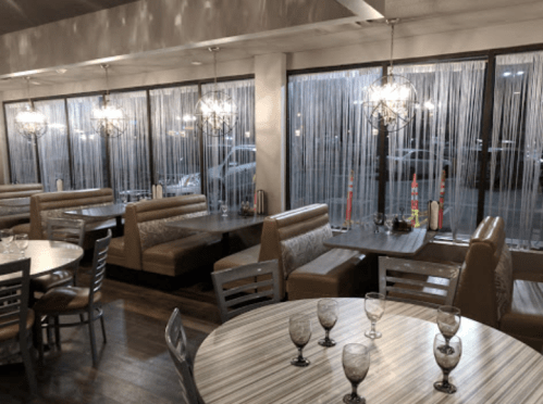 Interior of a modern restaurant with booths and tables, featuring decorative lighting and sheer curtains.
