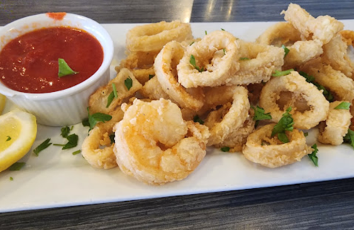 A plate of crispy fried calamari rings garnished with parsley, served with a side of marinara sauce and lemon wedges.