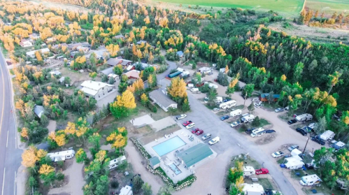 Aerial view of a campground with RVs, cabins, and a pool, surrounded by trees with autumn foliage.