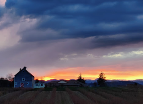 A rustic barn at sunset, with dramatic clouds and distant mountains in the background.