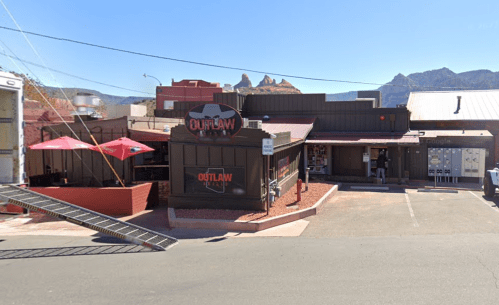 Exterior view of Outlaw restaurant with a sign, outdoor seating, and surrounding mountains in the background.