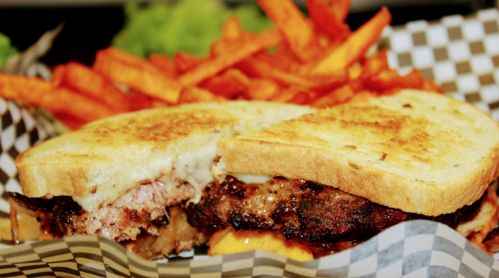 A close-up of a grilled sandwich with meat and cheese, served with crispy sweet potato fries on the side.
