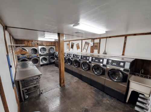 A spacious laundry room with multiple washing machines and dryers, stainless steel tables, and wooden paneling.