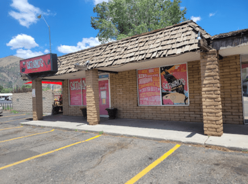 A brick building with a sloped roof, featuring colorful signs for "Saturdays" and a parking lot in front.