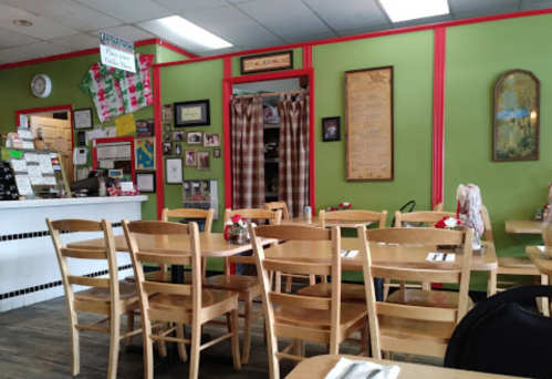 Cozy restaurant interior with green walls, wooden tables, and chairs, featuring decor and a welcoming atmosphere.