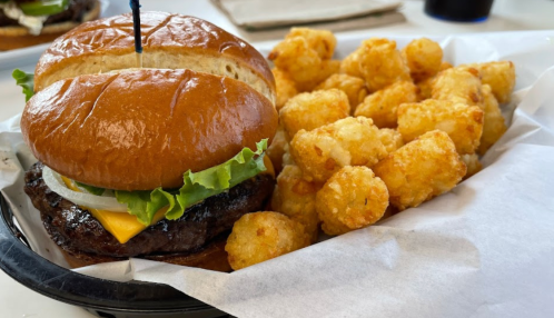 A juicy cheeseburger with lettuce and onion, served with a side of crispy tater tots in a black basket.