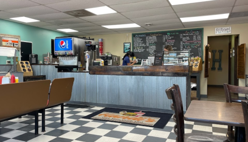 A cozy diner interior with a counter, menu boards, and checkered flooring, featuring a staff member serving customers.