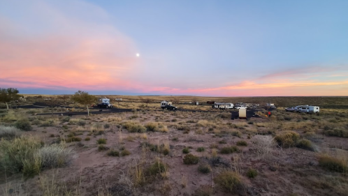 A serene desert landscape at sunset, featuring several RVs and a colorful sky with soft clouds.