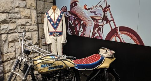 A vintage Harley-Davidson motorcycle displayed next to a white jumpsuit with a star design and a photo backdrop.