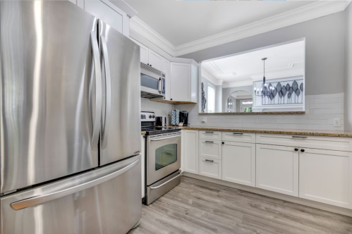 Modern kitchen featuring stainless steel appliances, white cabinetry, and a spacious layout with natural light.