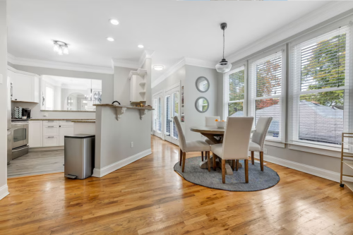 Bright, modern kitchen and dining area with a round table, four chairs, and large windows, featuring hardwood floors.