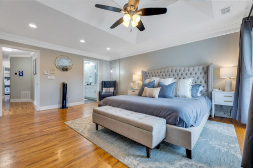 Spacious bedroom with a large bed, decorative pillows, a bench, and an en-suite bathroom visible in the background.