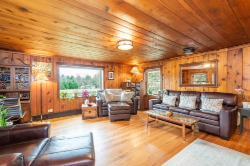 Cozy living room with wooden walls, leather furniture, and large windows overlooking greenery. Warm, inviting atmosphere.