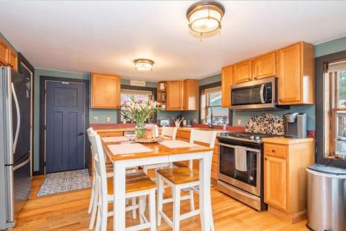 Bright kitchen with wooden cabinets, stainless steel appliances, a dining table, and flowers on the table.