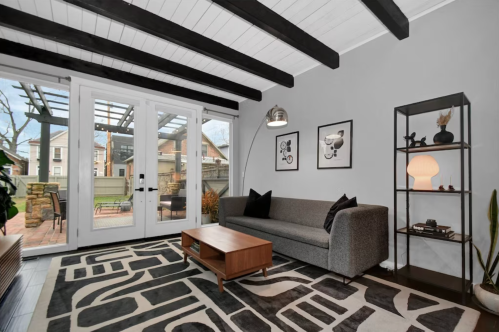 Cozy living room with a gray sofa, patterned rug, and large windows opening to an outdoor space. Modern decor accents.