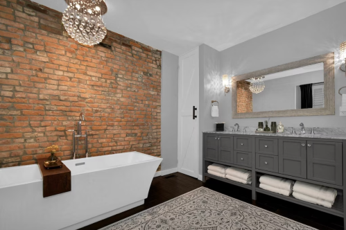 Modern bathroom featuring a freestanding tub, brick wall, double vanity, and elegant lighting.