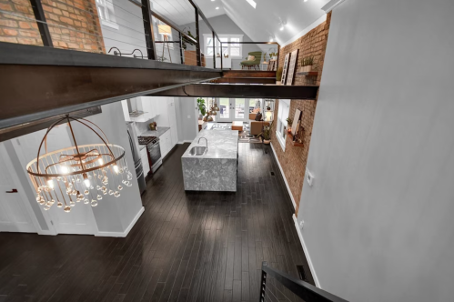 A spacious, modern interior with a view of a kitchen island, wooden floors, and a stylish chandelier.