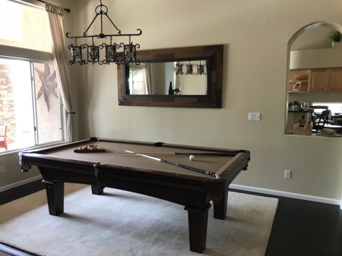 A spacious room featuring a billiards table, large mirror, and a window with natural light.