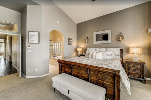 Cozy bedroom with a wooden bed, decorative pillows, and soft lighting, featuring a stylish bench and warm color palette.