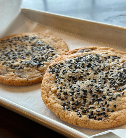 Two large cookies topped with black sesame seeds on a parchment-lined tray.