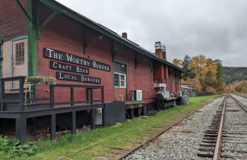 A red building with signs for "The Worthy Burger" and "Craft Beer, Local Burgers" next to a railway track.
