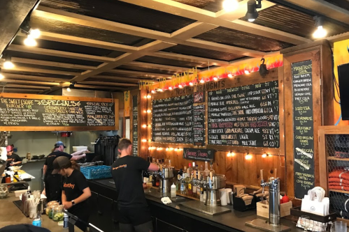A cozy café counter with a menu board, staff preparing drinks, and warm lighting.
