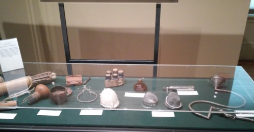 Display case featuring various historical medical instruments and bottles on a green surface.