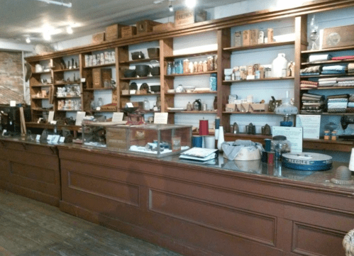 A vintage shop interior featuring wooden shelves filled with various items and a counter with display cases.