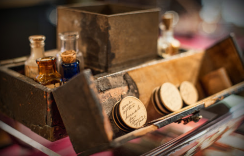 A vintage wooden box with small glass bottles and round coasters, displayed on a table.