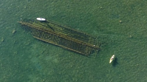 Aerial view of a sunken wooden structure in shallow water, with a kayak nearby.
