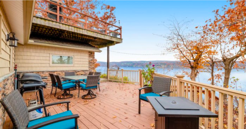 A scenic deck with outdoor seating, overlooking a lake surrounded by autumn foliage and clear blue skies.