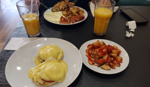 A table with two plates of breakfast: eggs Benedict, potatoes with ketchup, and a full breakfast with orange juice.