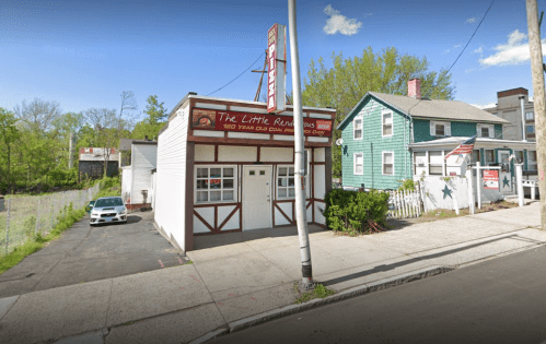 A small, quaint building labeled "The Little Reunions" with a parking area and nearby houses on a sunny day.