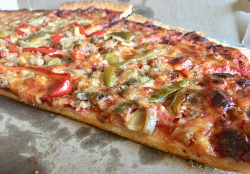 A close-up of a slice of pizza topped with sausage, peppers, and vegetables, resting in a pizza box.