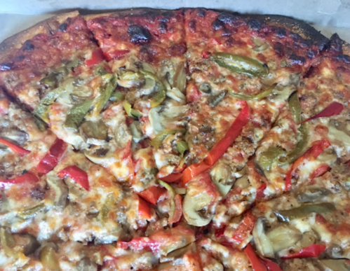 A close-up of a pizza topped with melted cheese, green and red peppers, and sausage, with a crispy crust.