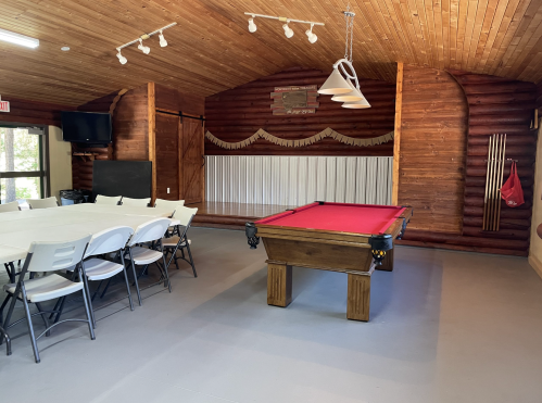 Interior of a rustic game room featuring a pool table, folding chairs, and wooden walls.