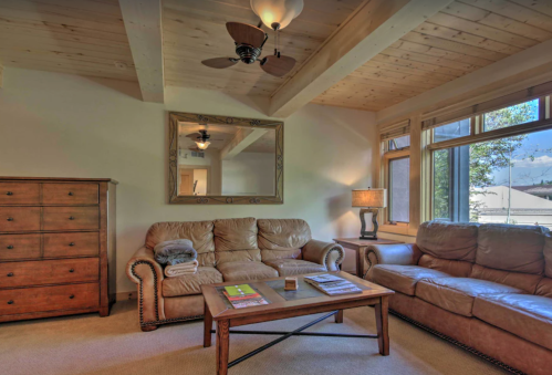 Cozy living room with wooden beams, a coffee table, two sofas, a dresser, and large windows letting in natural light.