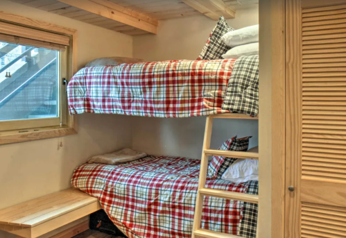Cozy bedroom with a bunk bed featuring plaid bedding and a window, wooden accents, and a small seating area.