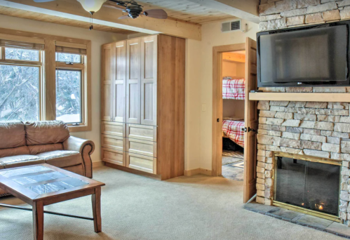 Cozy living room with a leather couch, stone fireplace, and a view of a bedroom with bunk beds.